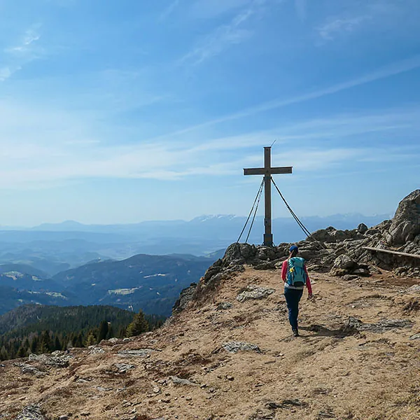 Person wandert Berggipfelkreuz entgegen