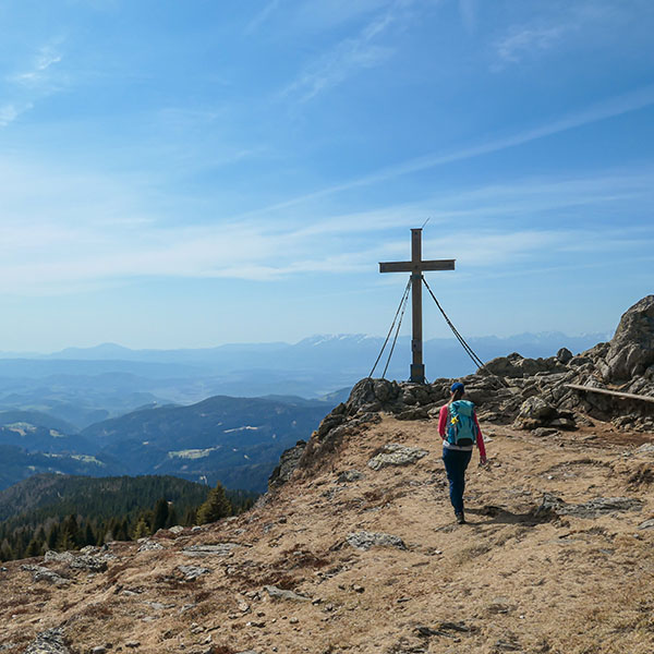 Person wandert in Richtung Gipfelkreuz auf Berggipfel